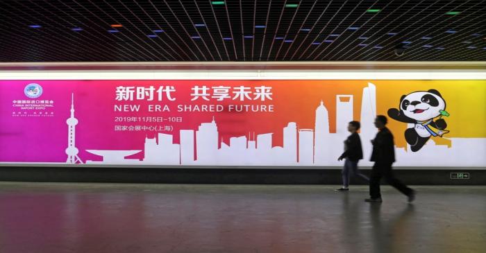 People walk past an advertisement for the upcoming China International Import Expo at a train