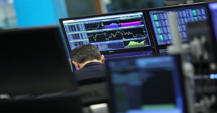 FILE PHOTO: A trader works as screens show market data at CMC markets in London