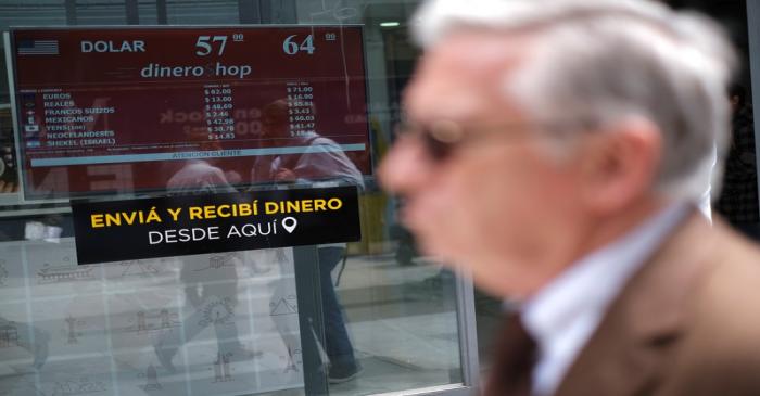 People walk past a screen showing currency exchange rates at a currency exchange shop in Buenos