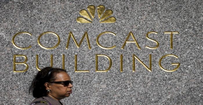 A woman walks past the NBC logo and Comcast at 30 Rockefeller Plaza in Manhattan, New York