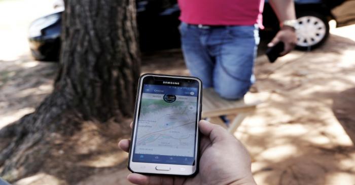 FILE PHOTO: Uber driver holds his cell phone showing the queue to pick up passengers departing