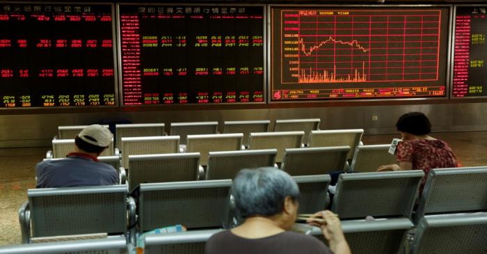 People sit in front of a board showing market information at a securities brokerage house in