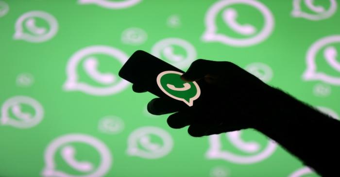 FILE PHOTO: A man poses with a smartphone in front of displayed Whatsapp logo in this