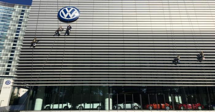 Workers clean the facade of a car showroom under a Volkswagen logo in Beijing