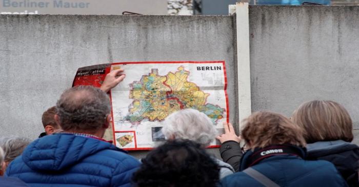 People watch a map of the divided West and East Berlin shown on remains of the Berlin Wall at