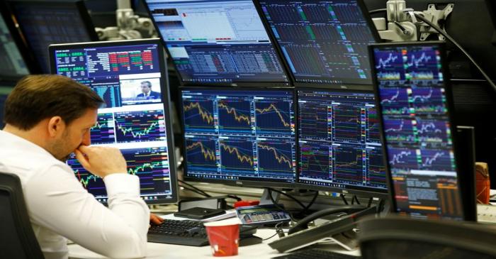 Traders work at their desks whilst screens show market data at CMC Markets in London