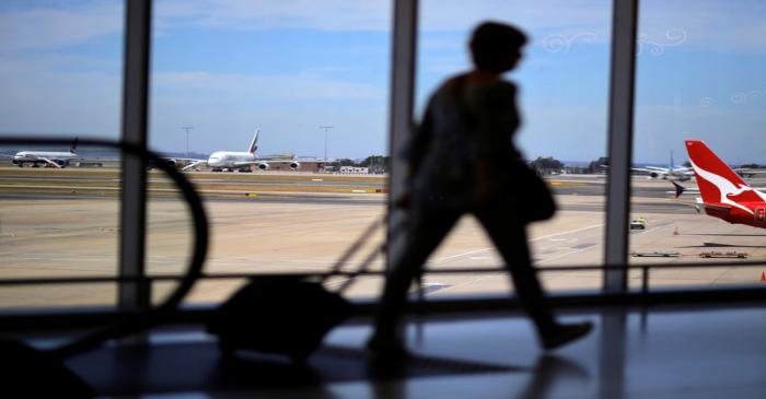 A passenger walks with their luggage towards a Qantas Airways plane at Sydney International