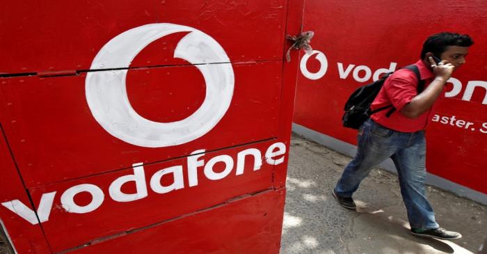 FILE PHOTO: Man speaks on his mobile phone as he walks past the logos of Vodafone painted on a