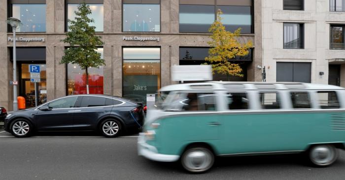 A Volkswagen oldtimer car drives past a Tesla Model X electric car recharging batteries in