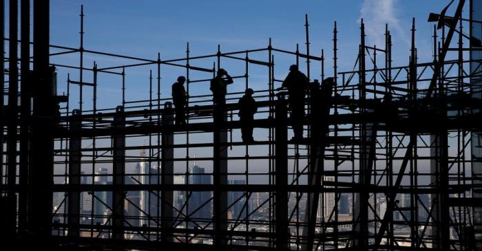 Construction workers are silhouetted while standing on scaffolding at the construction site of