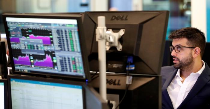 Traders work at their desks whilst screens show market data at CMC Markets in London