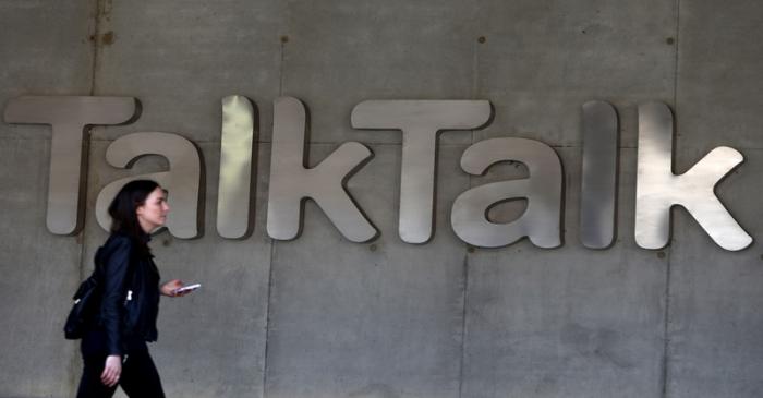 A woman carries her phone as she passes a branded logo outside the Talktalk headquarters in