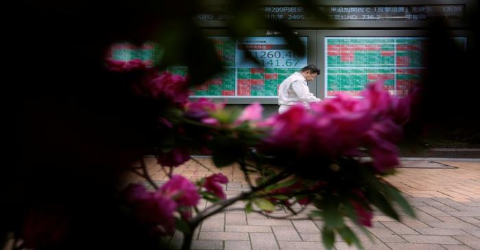 FILE PHOTO: A passerby walks past in front of a stock quotation board outside a brokerage in