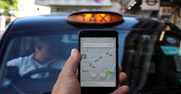 A photo illustration shows the Uber app and a black cab in London,