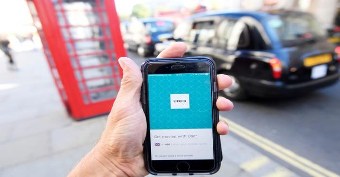 FILE PHOTO: A photo illustration shows a London taxi passing as the Uber app logo is displayed