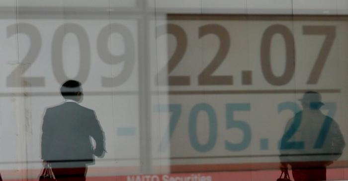 Men are reflected on an electronic board showing the Nikkei stock index outside a brokerage in