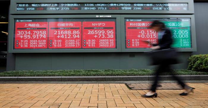 A woman walks past an electric screen showing world markets indices outside a brokerage in