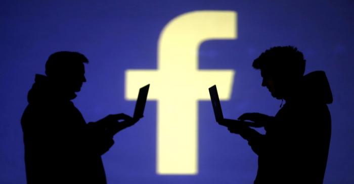 FILE PHOTO: Silhouettes of laptop users are seen next to a screen projection of Facebook logo
