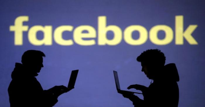 FILE PHOTO: Silhouettes of laptop users are seen next to a screen projection of Facebook logo