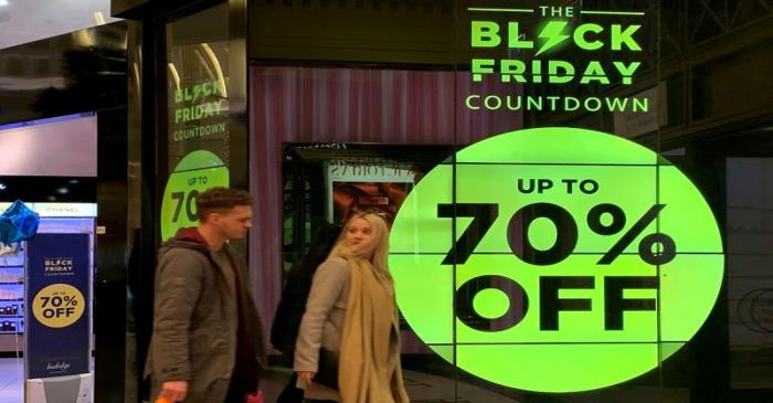 FILE PHOTO: People walk past a sign advertising Black Friday offers at a perfume store in