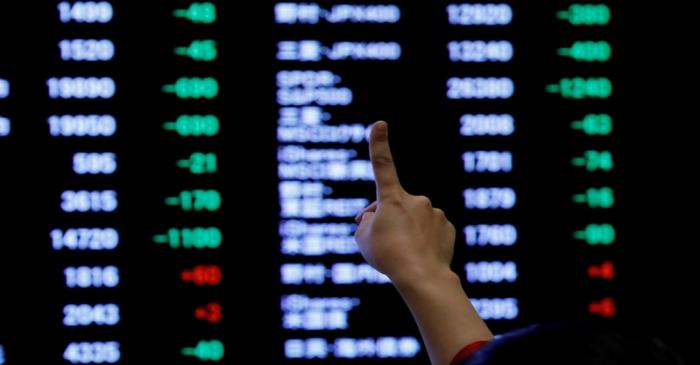 FILE PHOTO: A woman points to an electronic board showing stock prices as she poses in front of