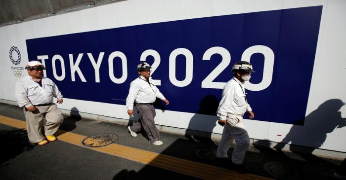 Construction workers walk past at a construction site of a building displaying Tokyo 2020