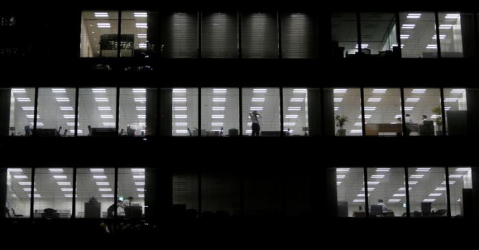 FILE PHOTO: A man using his mobile phone stands near a glass window at a building at a Tokyo