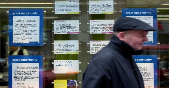 A man walks past job advertisements in the window of a recruitment office in central London