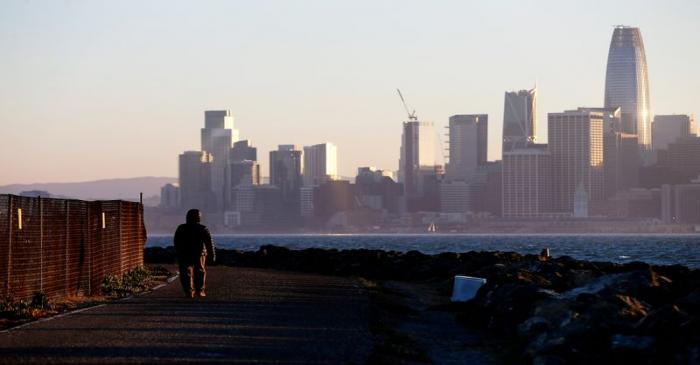 FILE PHOTO: The San Francisco skyline is seen behind a woman as she walks past a condemned area