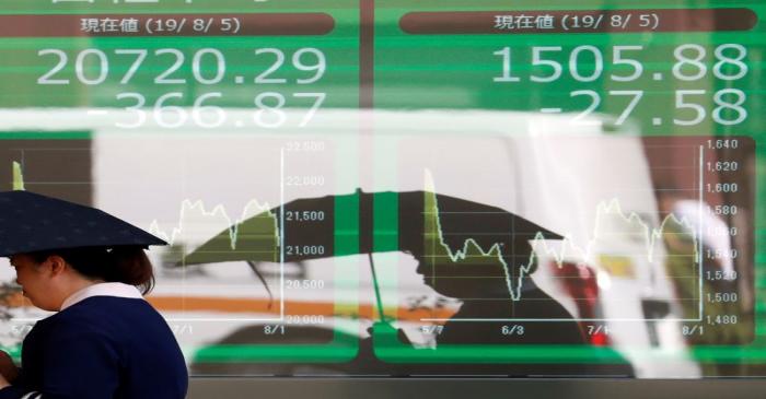 A woman walks past in front of an electric screen showing Japan's Nikkei share average outside