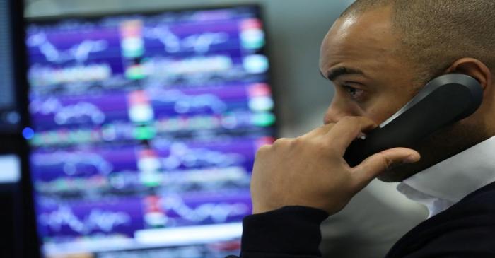 A trader works as screens show market data at CMC markets in London