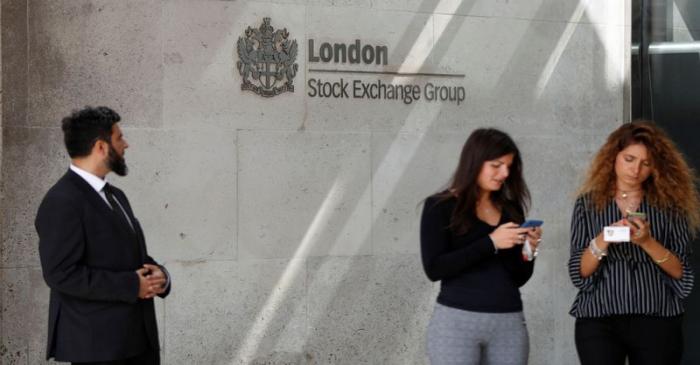 People check their mobile phones as they stand outside the entrance of the London Stock