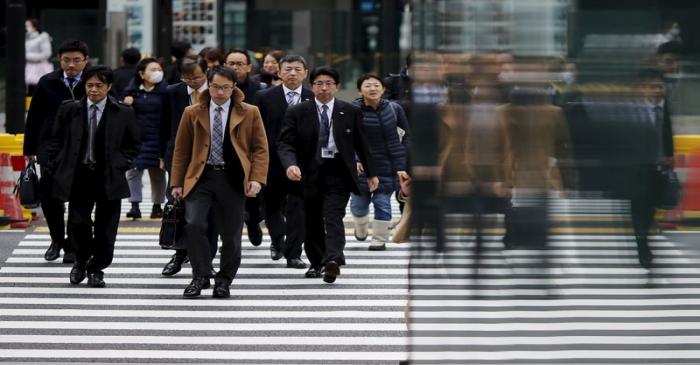 People are reflected on a wall as they cross a road at Tokyo's business district