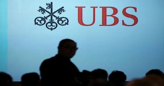 A man walks past a UBS logo projected on a screen in Singapore