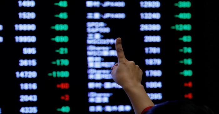 A woman points to an electronic board showing stock prices as she poses in front of the board