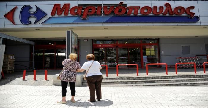 Two women stand in front of a Marinopoulos supermarket, while the Greek retail group