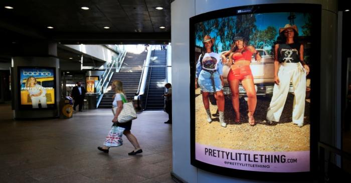 A shopper walks pass advertising billboards for Boohoo and for 'Pretty Little Things', a Boohoo