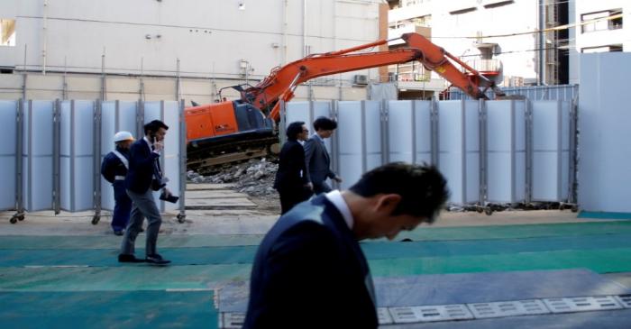 FILE PHOTO: Businessmen walk past heavy machinery at a construction site in Tokyo's business