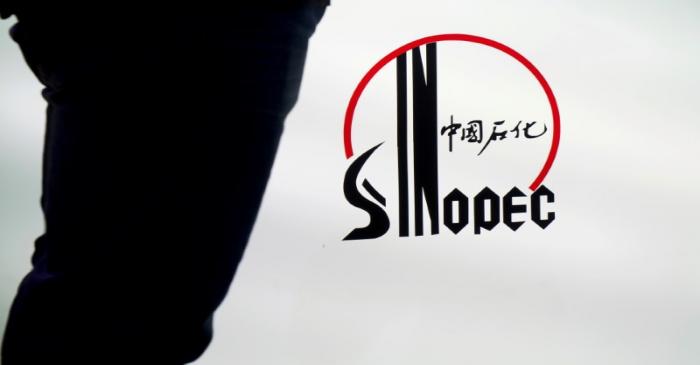 FILE PHOTO: Man stands next to a logo of Sinopec at an expo on rubber technology in Shanghai
