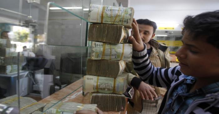 A customer receives bundles of Yemeni Riyal banknotes at an exchange company in Sanaa