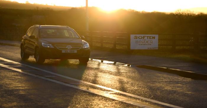 A car drives by a sign to 'soften the border' at sunset on the border bridge between County