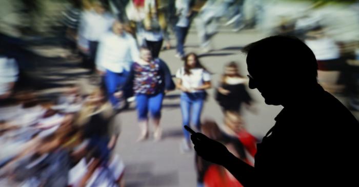 A man looks at data on his mobile as background with crowd of people walking is projected in