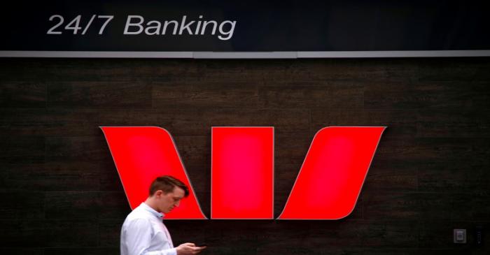 FILE PHOTO: A pedestrian looks at his phone as he walks past a logo for Australia's Westpac