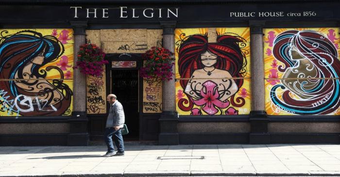 FILE PHOTO:  A pedestrian walks past a bordered up pub ahead of Notting Hill Carnival in London