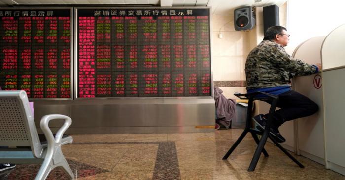 An investor sits next to a stock quotation board at a brokerage office in Beijing