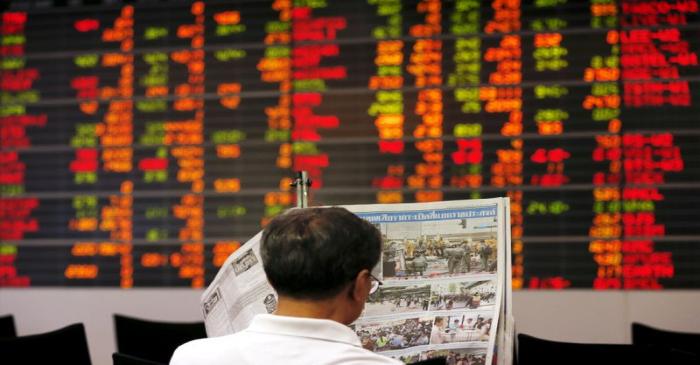 FILE PHOTO: A Thai investor reads a newspaper in front of an electronic board displaying live