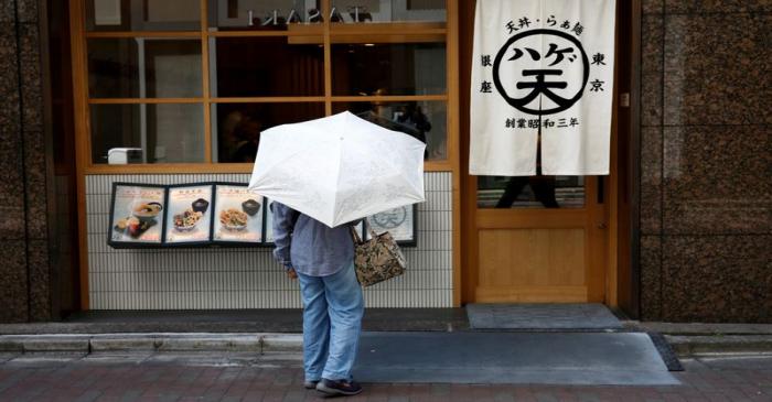 FILE PHOTO: A woman holding a parasol looks at a menu board in front of a restaurant at a