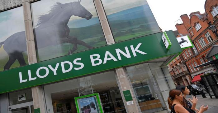 FILE PHOTO: A woman looks at her phone as she walks past a branch of Lloyds bank in London,