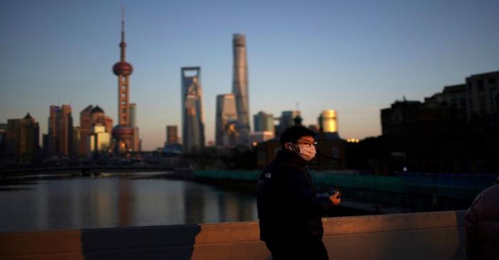 A man wearing a face mask walks on a bridge in front of the financial district of Pudong in
