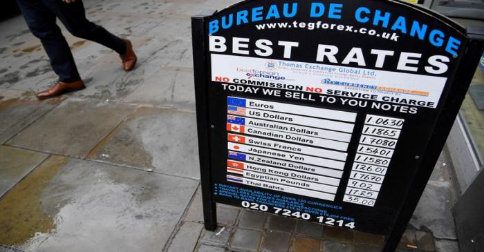 FILE PHOTO: A man walks past a board displaying buying and selling rates outside of a currency